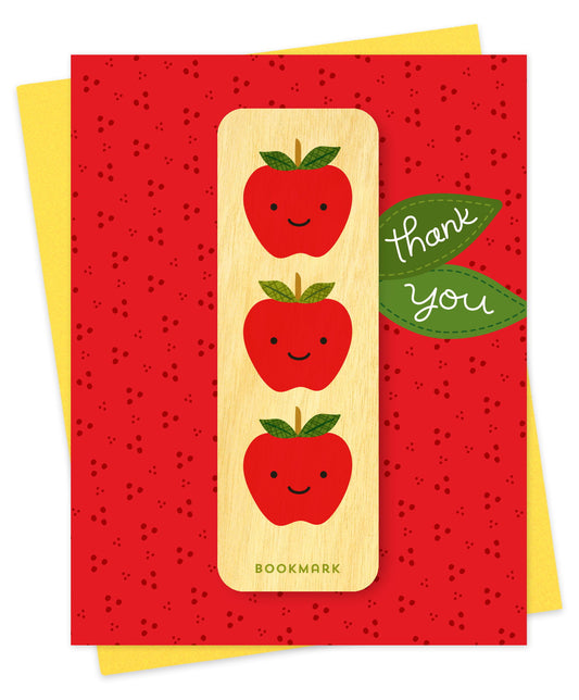 Folded thank you card with a bold red speckled background, thank you text on green leaves and a removable birch wood bookmark featuring three smiling apples. Pictured with a yellow envelope.