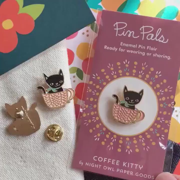 Front of enamel pin is a smiling black cat in a pink coffee cup with gold accents. Back of pin is gold with the Night Owl Paper Goods script logo. Pin is mounted on a backer card that says "Pin Pals - Enamel Pin Flair - Ready for wearing or sharing - COFFEE KITTY - by Night Owl Paper Goods" and is packaged in a clear bag.