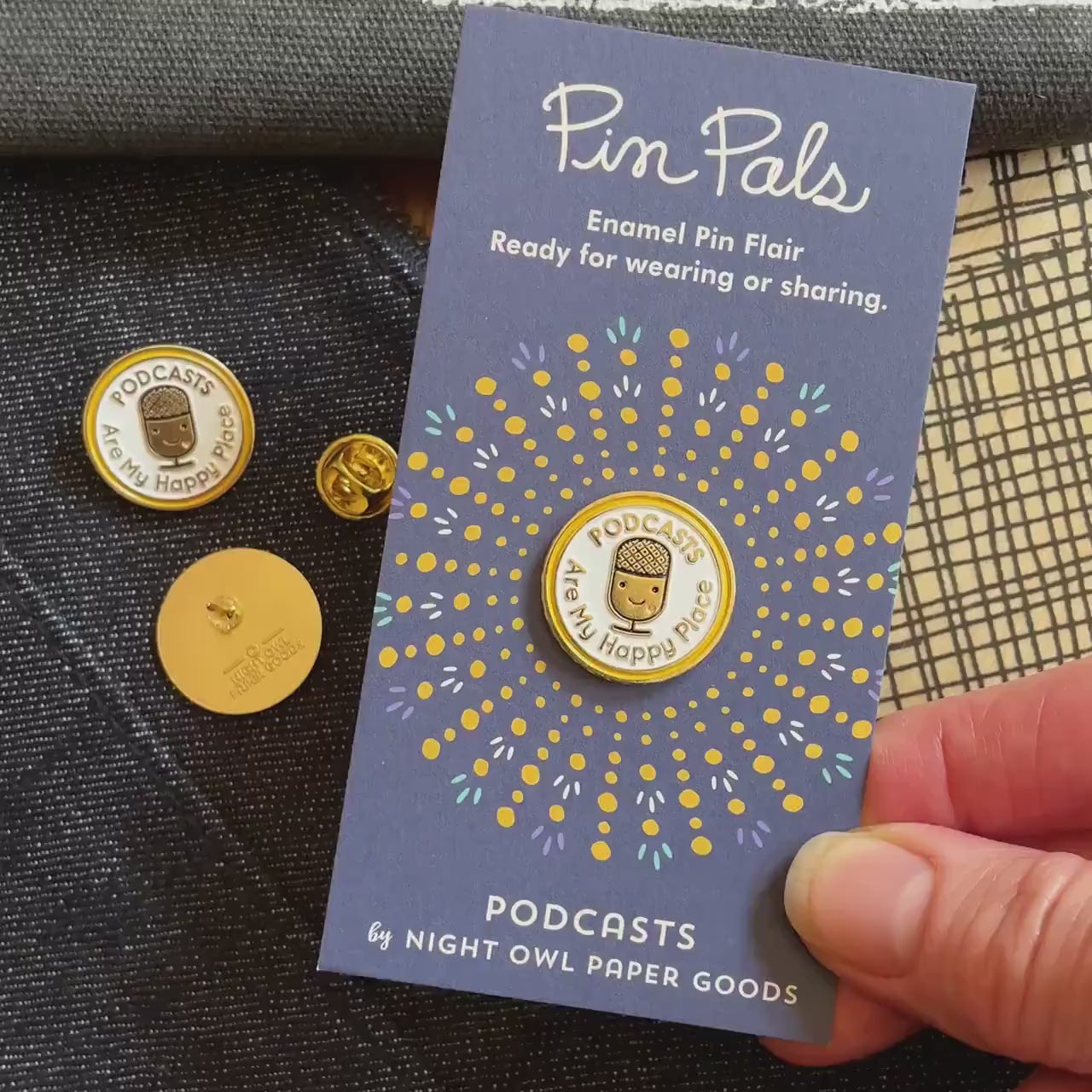 Front of enamel pin is a smiling microphone with "PODCASTS are my happy place" text and gold accents. Back of pin is gold with the Night Owl Paper Goods script logo. Pin is mounted on a backer card that says "Pin Pals - Enamel Pin Flair - Ready for wearing or sharing - PODCASTS - by Night Owl Paper Goods" and is packaged in a clear bag.