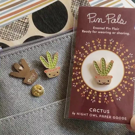 Front of enamel pin is smiling potted cactus with gold accents. Back of pin is gold with the Night Owl Paper Goods script logo. Pin is mounted on a backer card that says "Pin Pals - Enamel Pin Flair - Ready for wearing or sharing - CACTUS - by Night Owl Paper Goods" and is packaged in a clear bag.
