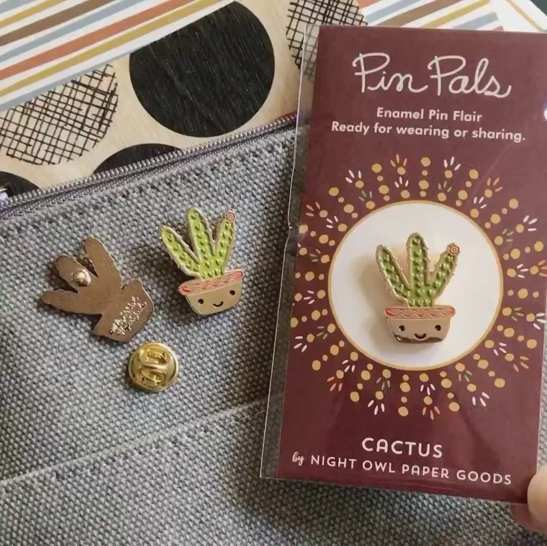 Front of enamel pin is smiling potted cactus with gold accents. Back of pin is gold with the Night Owl Paper Goods script logo. Pin is mounted on a backer card that says "Pin Pals - Enamel Pin Flair - Ready for wearing or sharing - CACTUS - by Night Owl Paper Goods" and is packaged in a clear bag.