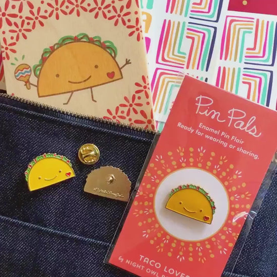Front of enamel pin is a smiling taco with a red heart and gold accents. Back of pin is gold with the Night Owl Paper Goods script logo. Pin is mounted on a backer card that says "Pin Pals - Enamel Pin Flair - Ready for wearing or sharing - TACO LOVER - by Night Owl Paper Goods" and is packaged in a clear bag.