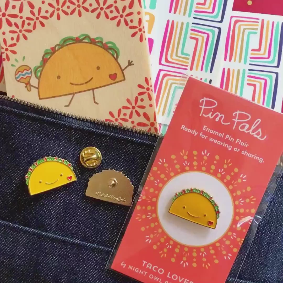 Front of enamel pin is a smiling taco with a red heart and gold accents. Back of pin is gold with the Night Owl Paper Goods script logo. Pin is mounted on a backer card that says "Pin Pals - Enamel Pin Flair - Ready for wearing or sharing - TACO LOVER - by Night Owl Paper Goods" and is packaged in a clear bag.