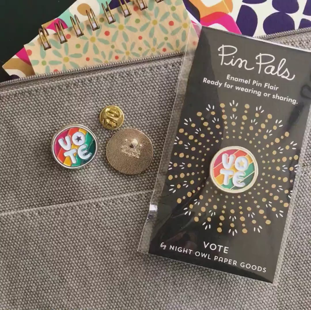 Front of enamel pin is rainbow striped with VOTE text, a small star in the middle of the "O" and gold accents. Back of pin is gold with the Night Owl Paper Goods script logo. Pin is mounted on a backer card that says "Pin Pals - Enamel Pin Flair - Ready for wearing or sharing - VOTE - by Night Owl Paper Goods" and is packaged in a clear bag.