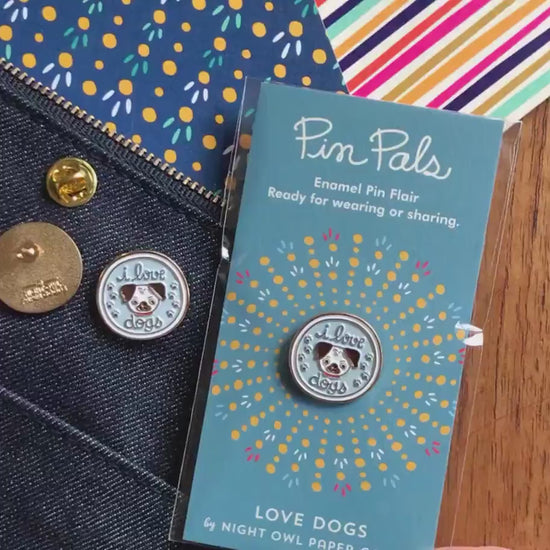I Love Dogs enamel pin in packaging, shown front and back. Light blue dog lover lapel pin with cute dog face illustration.