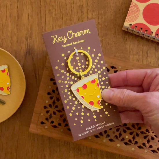 Front of enamel keychain is a smiling piece of pepperoni pizza with "I live for pizza night" text and gold accents. Keychain is mounted on a backer card that says "Key Charm - Enamel Keychain - Pizza Night by Night Owl Paper Goods" and is packaged in a clear box.