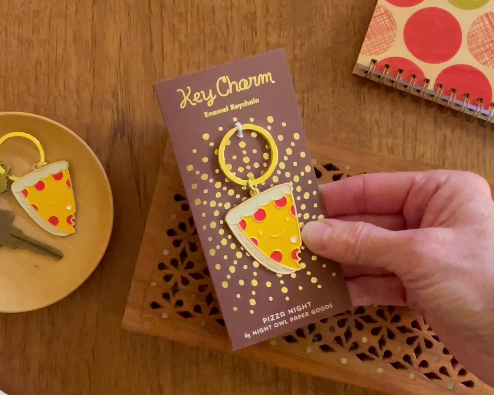 Front of enamel keychain is a smiling piece of pepperoni pizza with "I live for pizza night" text and gold accents. Keychain is mounted on a backer card that says "Key Charm - Enamel Keychain - Pizza Night by Night Owl Paper Goods" and is packaged in a clear box.