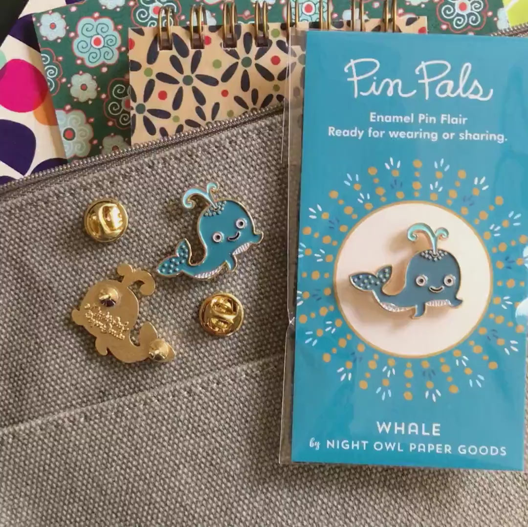 Front of enamel pin is a smiling blue whale with gold accents. Back of pin is gold with the Night Owl Paper Goods script logo. Pin is mounted on a backer card that says "Pin Pals - Enamel Pin Flair - Ready for wearing or sharing - WHALE - by Night Owl Paper Goods" and is packaged in a clear bag.