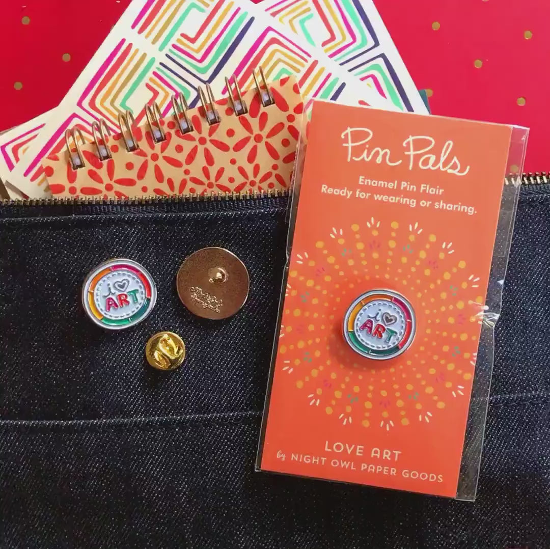 Front of enamel pin is a color wheel with "I heart art" text and gold accents. Back of pin is gold with the Night Owl Paper Goods script logo. Pin is mounted on a backer card that says "Pin Pals - Enamel Pin Flair - Ready for wearing or sharing - LOVE ART - by Night Owl Paper Goods" and is packaged in a clear bag.
