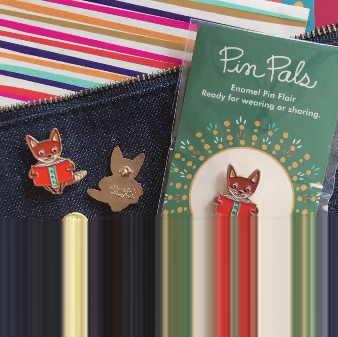 Front of enamel pin is a fox reading a book with gold accents and a small white heart. Back of pin is gold with the Night Owl Paper Goods script logo. Pin is mounted on a backer card that says "Pin Pals - Enamel Pin Flair - Ready for wearing or sharing - READING FOX - by Night Owl Paper Goods" and is packaged in a clear bag.