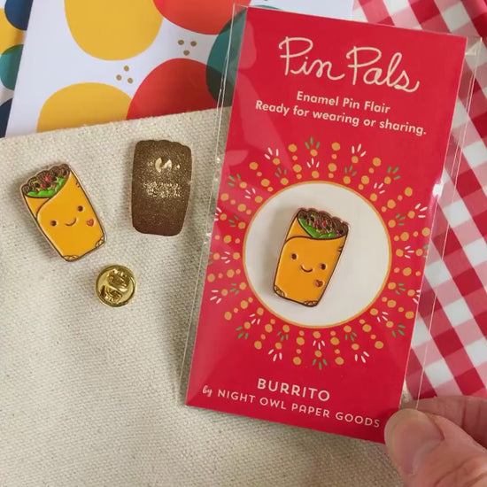 Front of enamel pin is a smiling burrito with a small red heart and gold accents. Back of pin is gold with the Night Owl Paper Goods script logo. Pin is mounted on a backer card that says "Pin Pals - Enamel Pin Flair - Ready for wearing or sharing - BURRITO - by Night Owl Paper Goods" and is packaged in a clear bag.